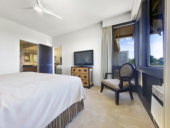 Ein Hotelzimmer mit einem Bett, einem Fernseher, einem Sessel, einem Schminktisch und einem Fenster mit Vorhängen.