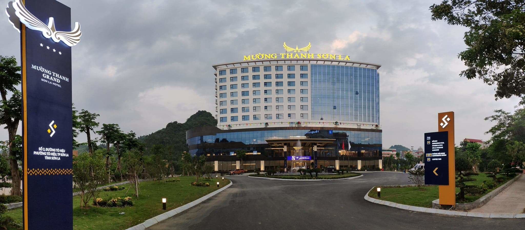 A hotel with a modern glass facade, a prominent sign reading "MUONG THANH SONA HOTEL," and a landscaped entrance area.