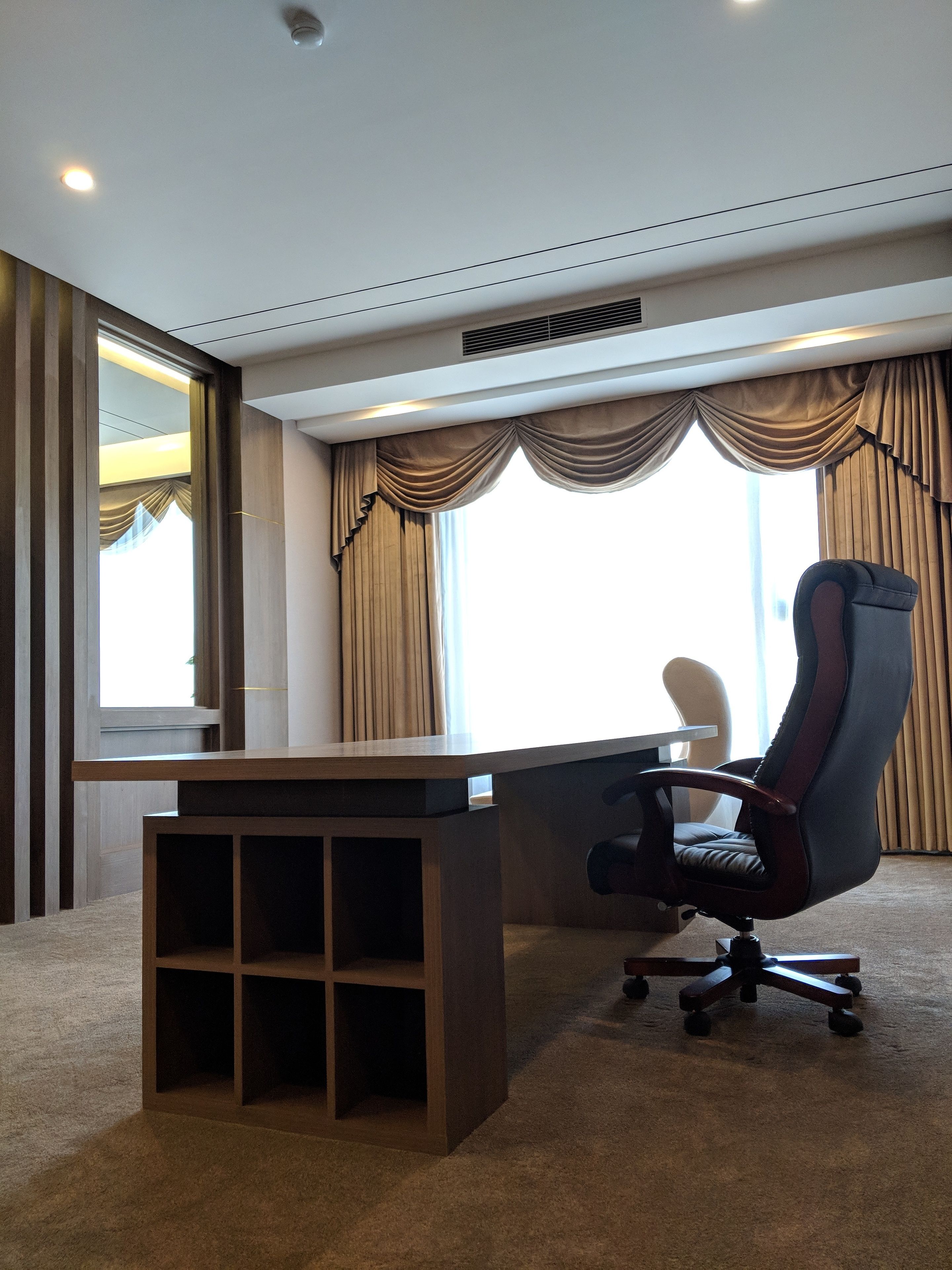 A modern office space with a wooden desk, a black office chair, and a large window with curtains.