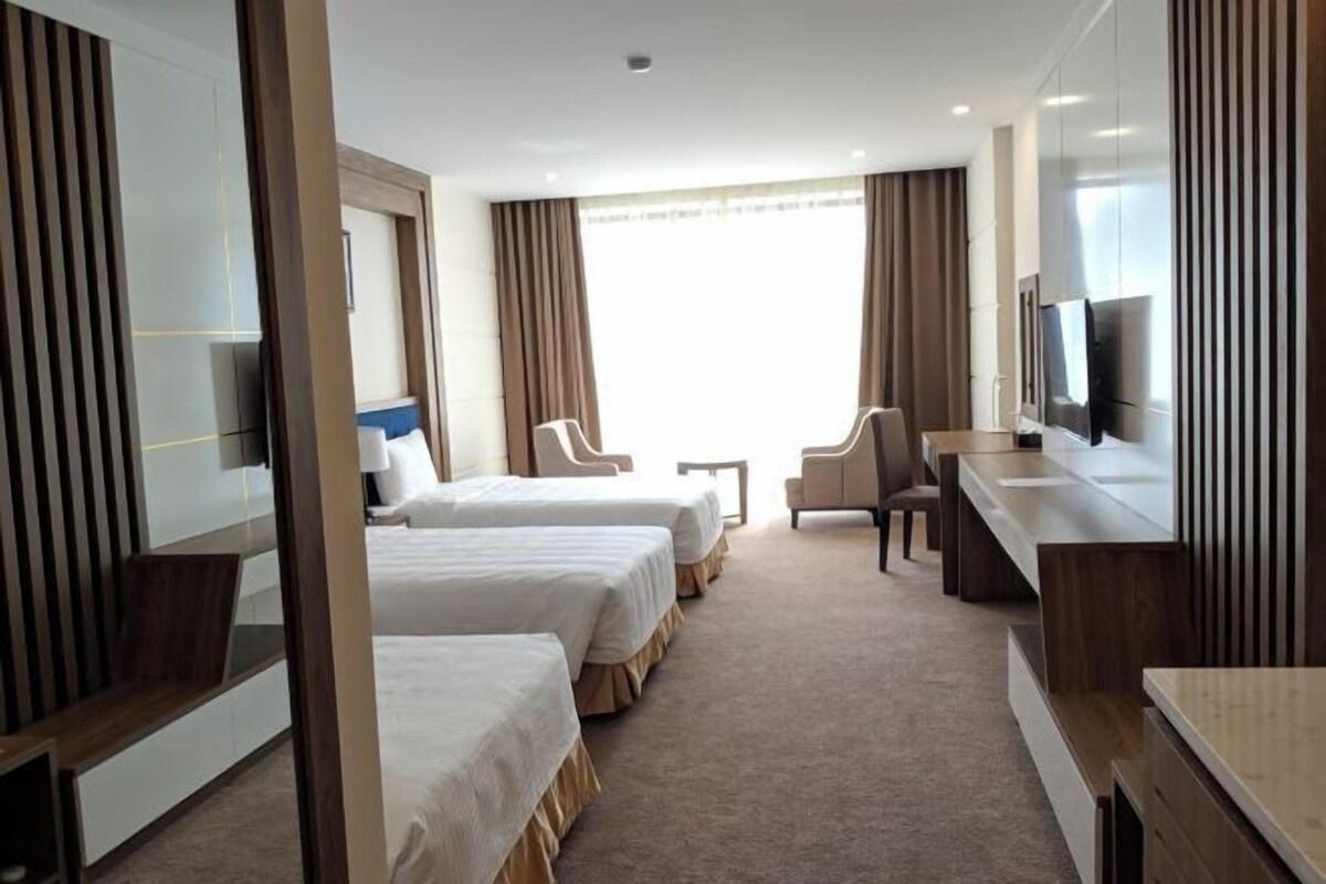 A hotel room with two beds, a desk, a chair, and a TV.