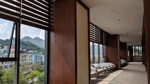 Ein modernes Hotelzimmer mit großen Fenstern, Blick auf die Stadt und einer Sitzecke mit Sofas.
