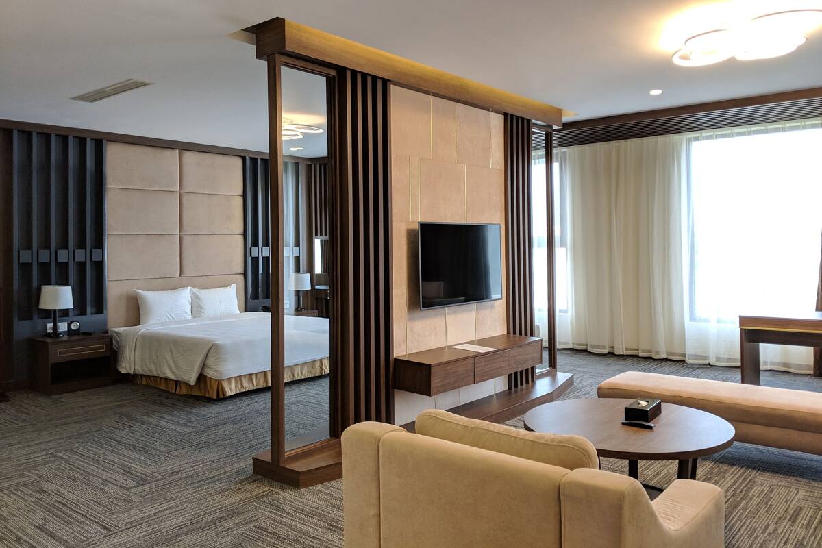 Una habitación de hotel con cama, televisión, escritorio, sofá y un ventanal grande.