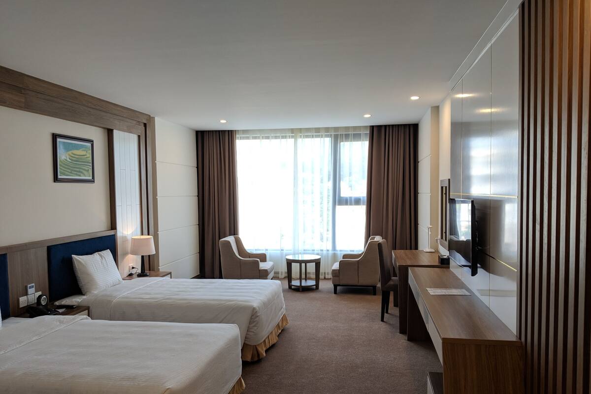 Habitación de hotel con dos camas, un escritorio, una silla, un televisor y una ventana con cortinas.