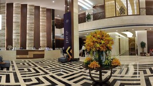 Eine moderne Hotelhalle mit einer Rezeption, einer großen Blumendekoration und einem strukturierten Boden.
