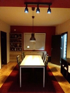 A dining area with a table and chairs, a pendant light, a bookshelf, and a refrigerator. - Grande House (Skopje)