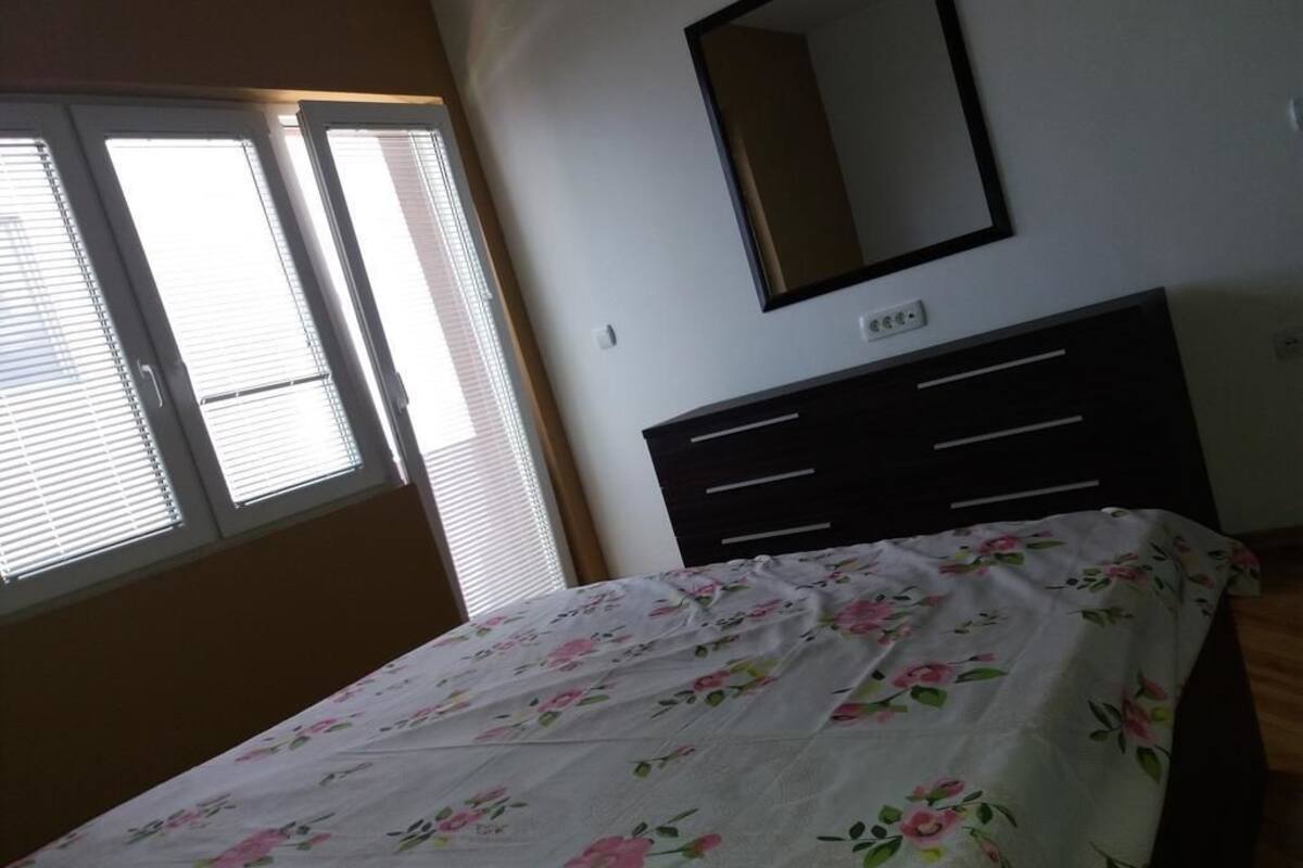 Ein Schlafzimmer mit Bett, Kommode, Spiegel und einem Fenster mit Jalousien.