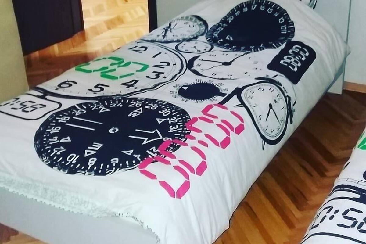 Ein Bett mit weißer Matratze, verziert mit Uhrendarstellungen und einem rosafarbenen Herz.