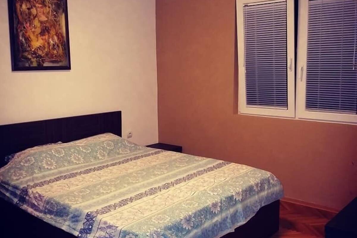 Ein Schlafzimmer mit Bett, einem Bild an der Wand und einem Fenster mit Jalousien.
