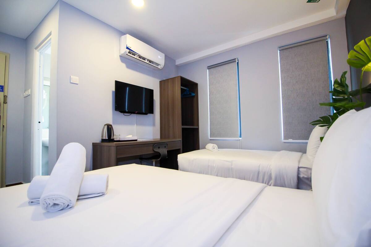 A hotel room with two beds, a desk, a flat-screen TV, an air conditioning unit, and a window with a view.