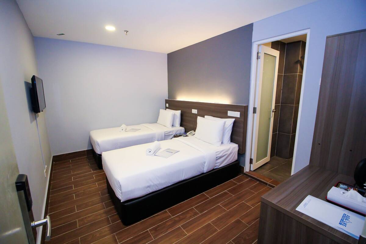 A hotel room with two single beds, a wooden floor, a small desk with a phone, and a mirror.