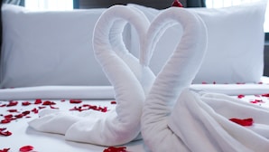 Un lit avec du linge de lit blanc et une serviette pliée en forme de cœur.
