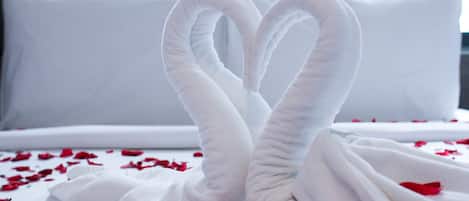 A bed with white linens and a heart-shaped towel arrangement.