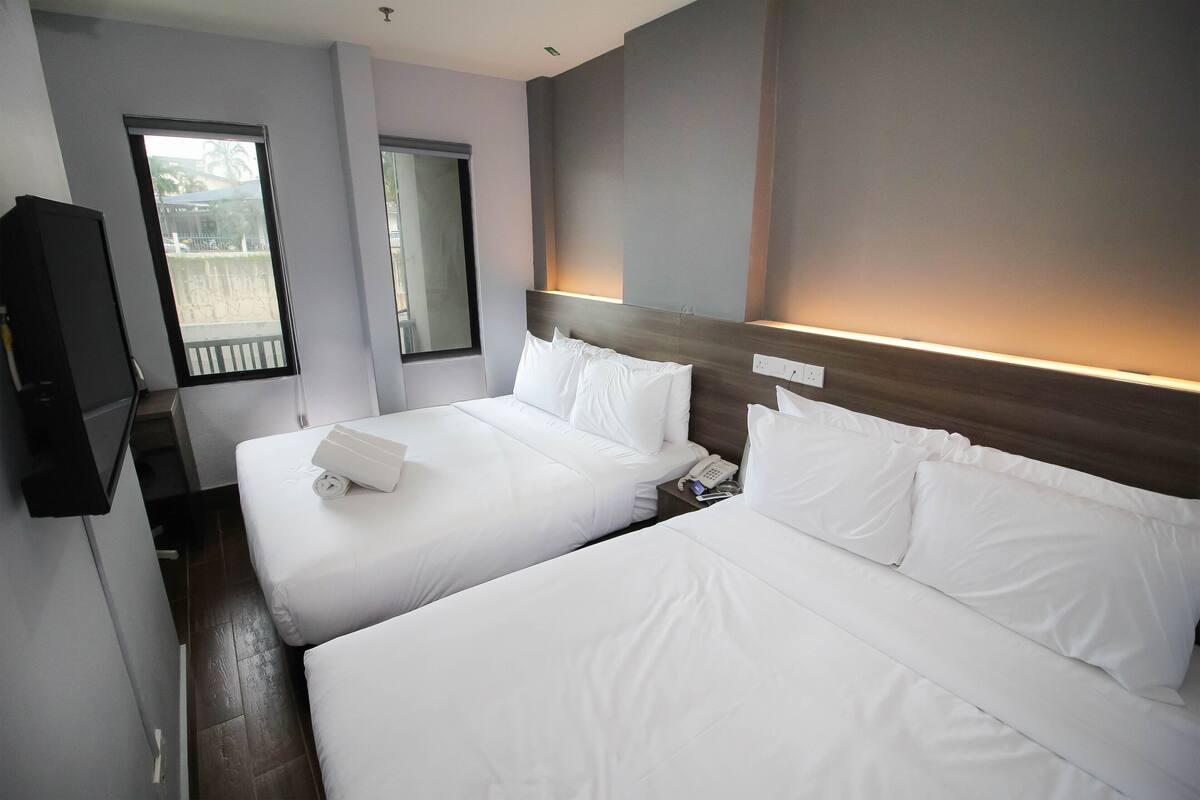 A hotel room with two beds, a TV, and a window with a view of the outside.