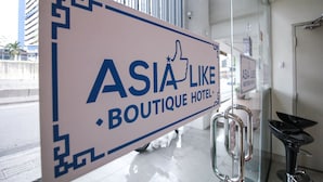 Une enseigne pour l'hôtel « Asia Like Boutique Hotel », avec une bordure géométrique et un pictogramme représentant un pouce levé.