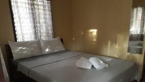 A neatly made bed with white linens and pillows, a pair of folded towels on the bed, and a window with sheer curtains allowing natural light to enter the room. - Port Barton DIY (San Vicente)