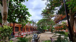 A courtyard with a dirt ground, surrounded by buildings with red and orange facades, and various potted plants. - Port Barton DIY (San Vicente)
