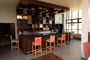 A bar area with a counter, bar stools, and shelves with glasses and bottles.