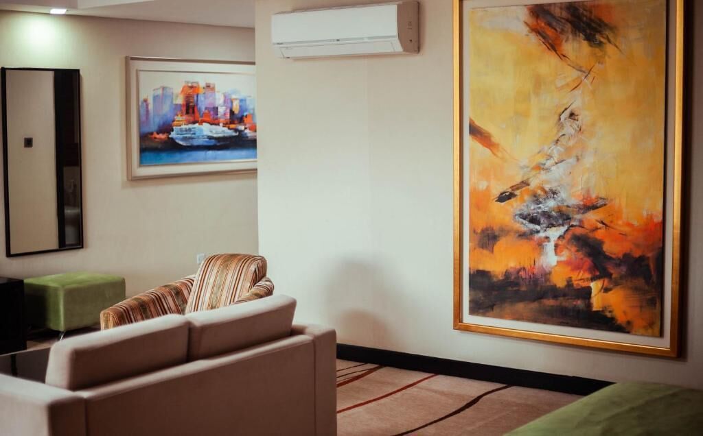 A hotel lobby with a sofa, a green ottoman, a framed cityscape painting, and an abstract painting.