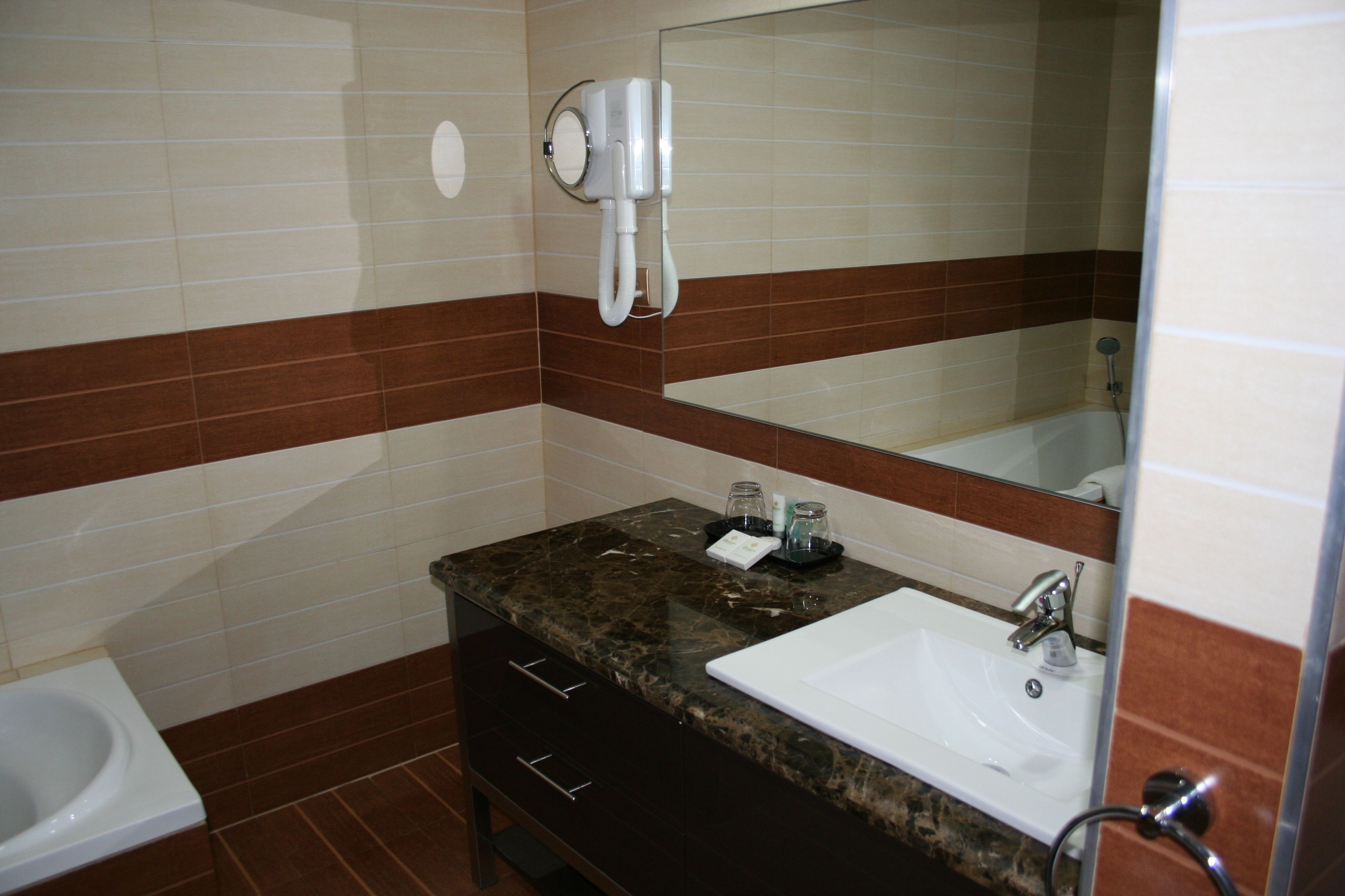 A bathroom with a white sink, dark marble countertop, and a hairdryer mounted on the wall.
