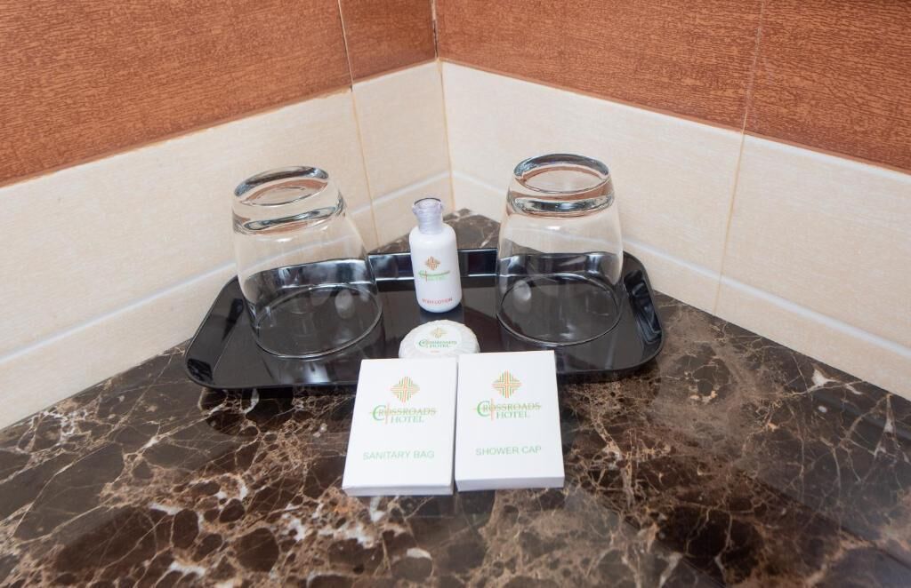 A bathroom counter with a marble surface, two glass shower caddies, a bottle of shampoo, and two boxes labeled 'Crossroads Hotel.'