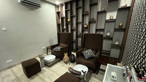 A modern living room with two brown armchairs, a white coffee table, a small white table, and a built-in shelving unit with decorative items. - Crossroads Hotel Blantyre (Blantyre)