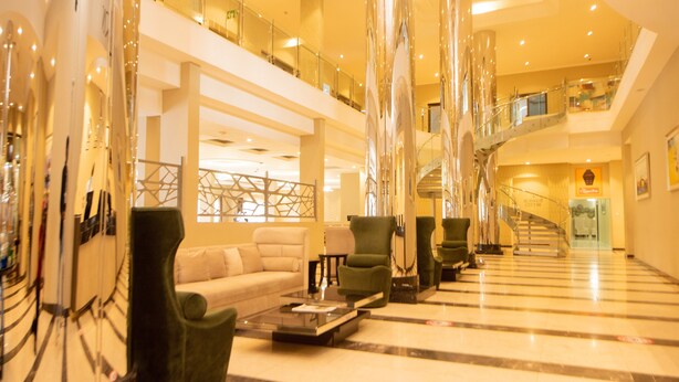A spacious lobby with a high ceiling, a central staircase, and a seating area with green armchairs and a sofa. - Crossroads Hotel Blantyre (Blantyre)
