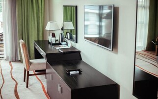 Una camera d'albergo con scrivania, sedia, due lampade, uno specchio e un quadro appeso al muro.