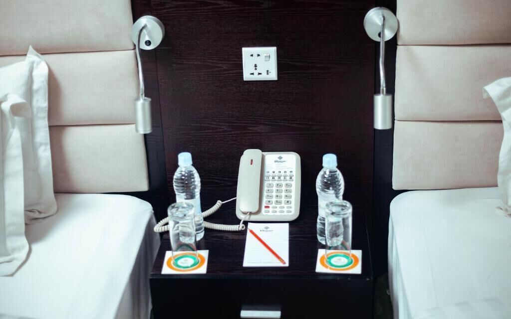 Habitación de hotel con cama, mesita de noche con teléfono, dos botellas de agua y un enchufe.