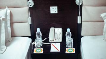 Habitación de hotel con cama, mesita de noche con teléfono, dos botellas de agua y un enchufe.