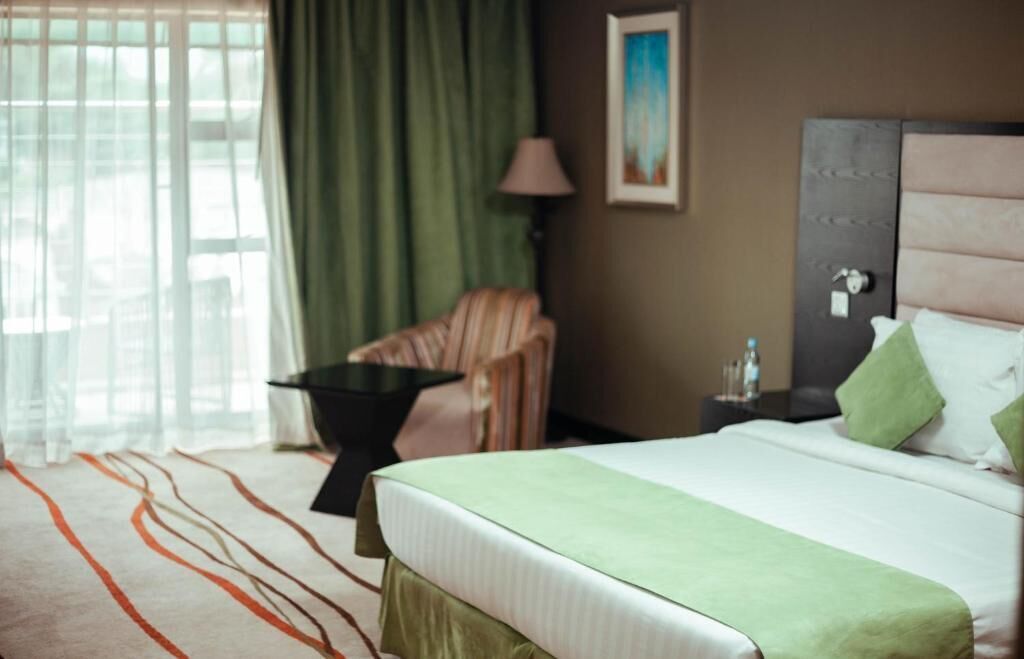 A hotel room with a bed, a chair, a nightstand, a lamp, and a painting on the wall.