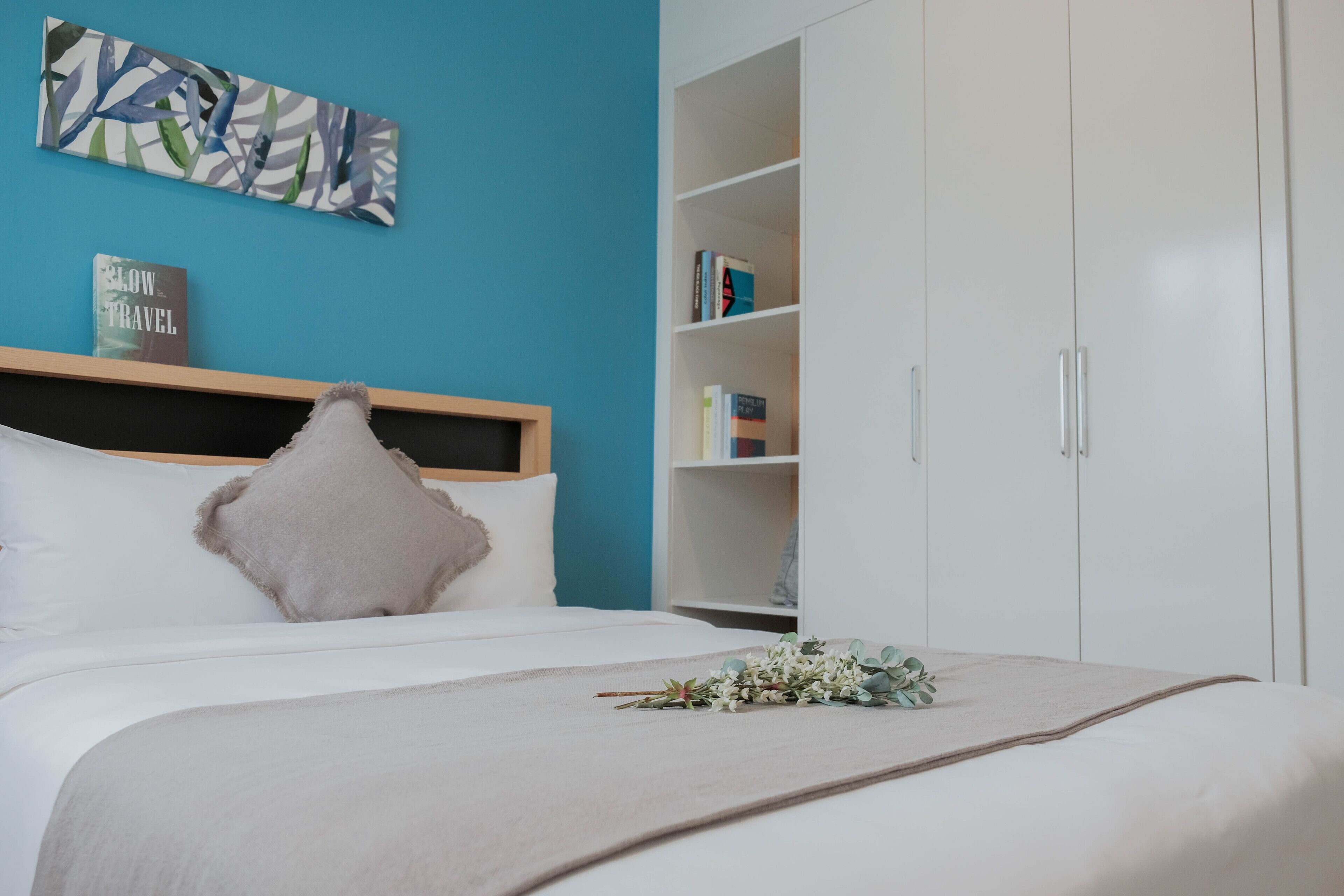 A neatly arranged bedroom with a bed, a bookshelf, and a wall art piece.