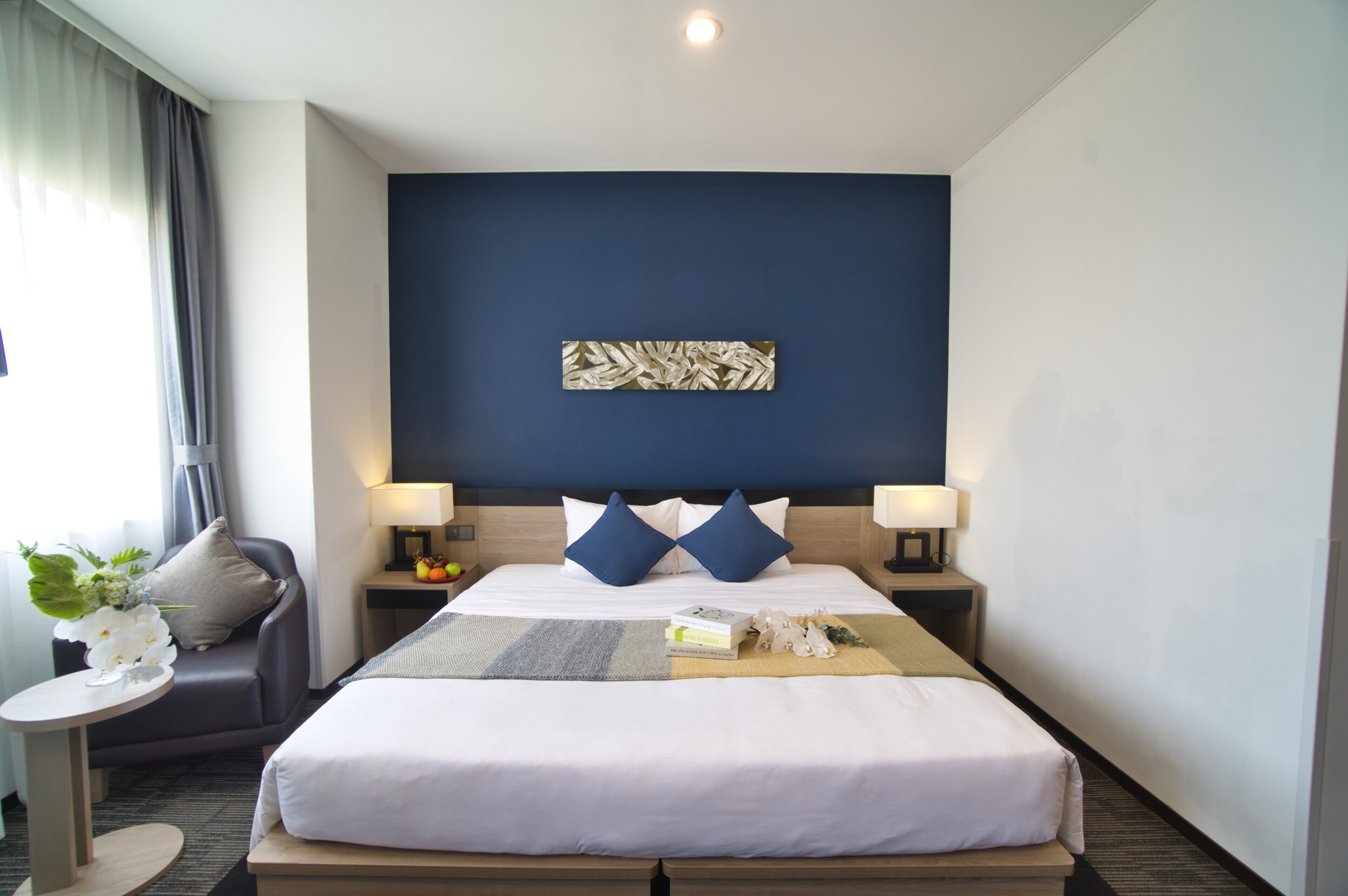 A hotel room with a large bed, two bedside tables with lamps, a small side table with a plant, and a wall-mounted artwork.