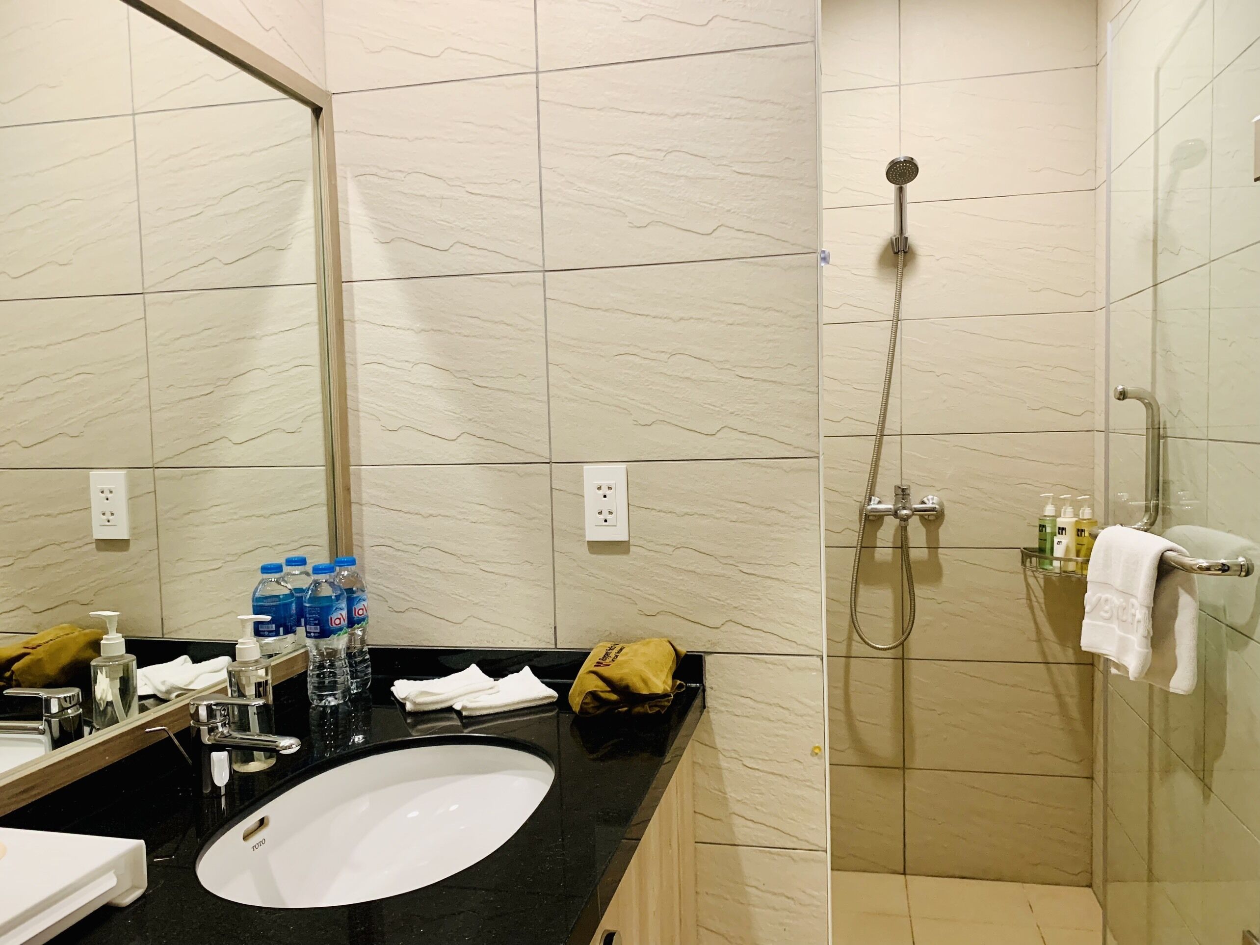 A bathroom with a white sink, a mirror, a shower with a handheld showerhead, and toiletries on the counter.