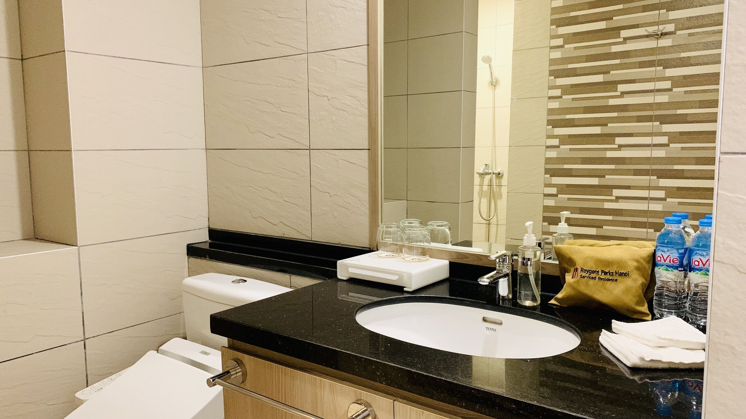 A modern bathroom with a black countertop, white sink, and a mirror. There are toiletries and a towel on the counter.