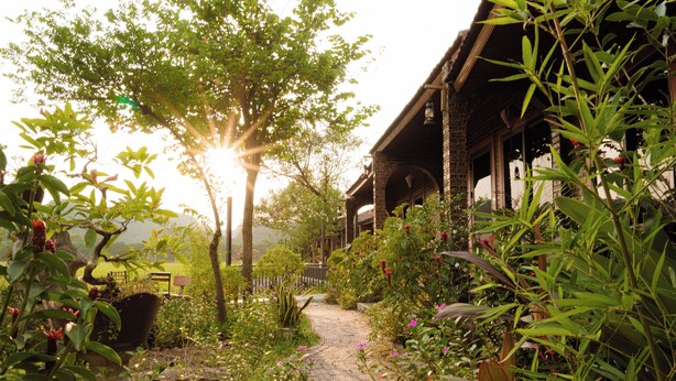 A garden pathway leading to a traditional building with a brick facade and wooden beams. - Heritage Soul Bungalow Tam Coc (Nam Hoa Lu)