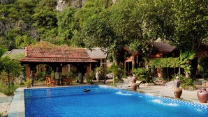 A swimming pool with a tiled edge, surrounded by lush greenery and traditional architecture. - Heritage Soul Bungalow Tam Coc (Nam Hoa Lu)