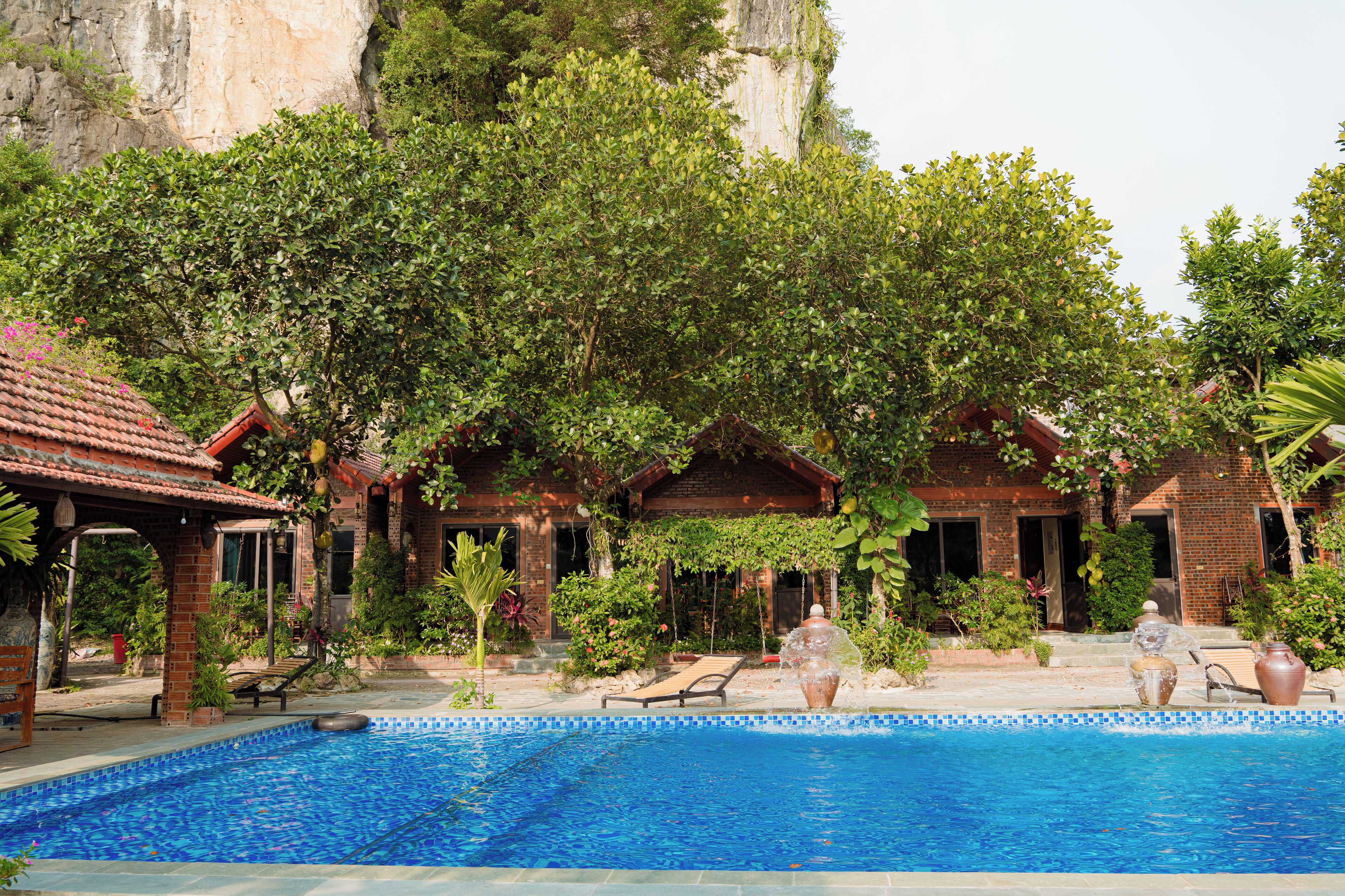 A pool area with a clear view of the surrounding architecture, including a brick building and a large rock formation.