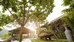 A covered outdoor area with a wooden structure, stone pathway, and lush greenery. - Heritage Soul Bungalow Tam Coc (Nam Hoa Lu)