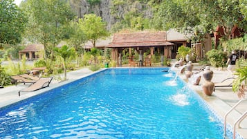 Una piscina al aire libre, sombrillas, sillones reclinables de piscina