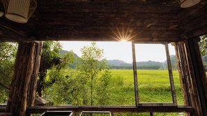 A rustic wooden interior with a large window overlooking a green field and mountains. - Heritage Soul Bungalow Tam Coc (Nam Hoa Lu)