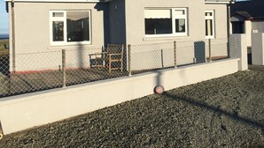 Uma casa de dois andares com fachada cinza, telhado escuro e entrada com calçada de brita.