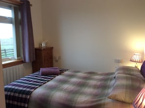 A bedroom with a bed, a dresser, a lamp, and a window with curtains. - The Homer (Kilmuir)