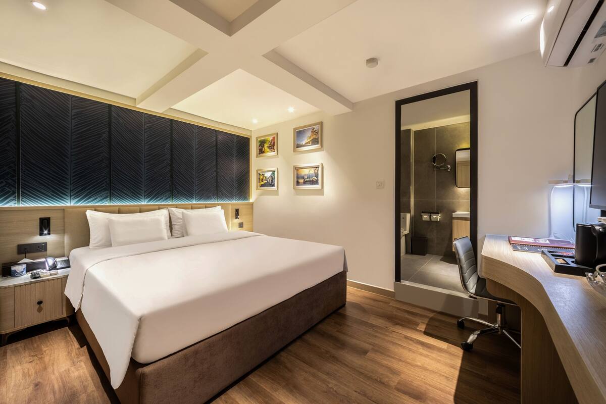 Habitación de hotel moderna con una cama grande, un escritorio con silla, un espejo y obras de arte en las paredes.