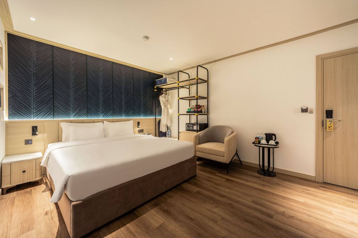Una habitación de hotel moderna con una cama grande, una silla, una mesita con cafetera y un armario.