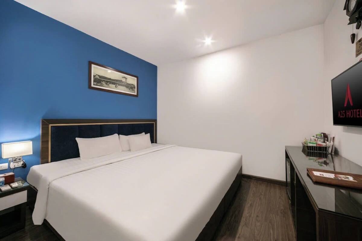 Habitación de hotel con una cama grande, un escritorio, una silla, un televisor y un cuadro en la pared.