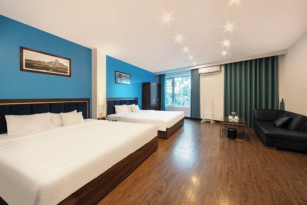 Habitación de hotel con dos camas, un sofá, un escritorio y un ventanal con cortinas.