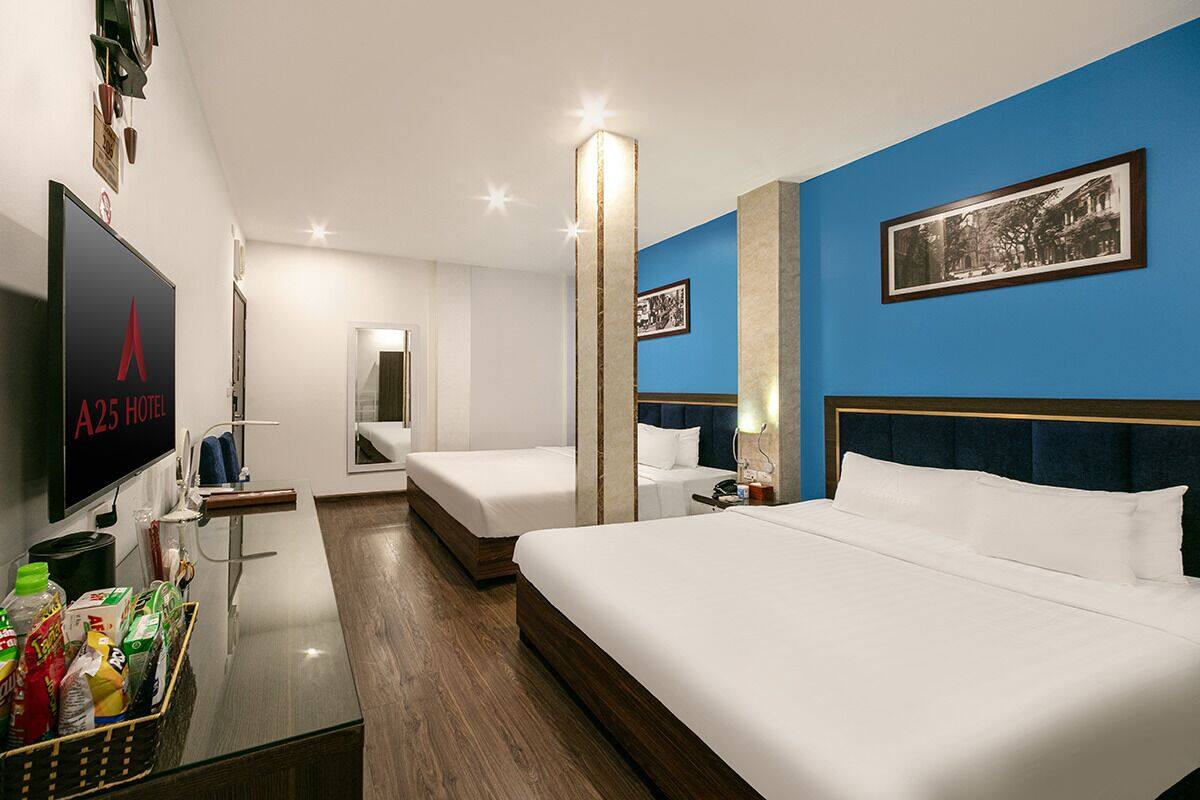 Una habitación de hotel con una cama grande, una cama más pequeña, un escritorio con televisor y un cuadro colgado en la pared.
