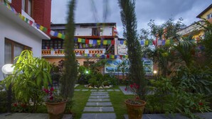 A courtyard with a stone pathway leading to a building entrance, surrounded by potted plants and greenery. - Hotel Dream City (Kathmandu)