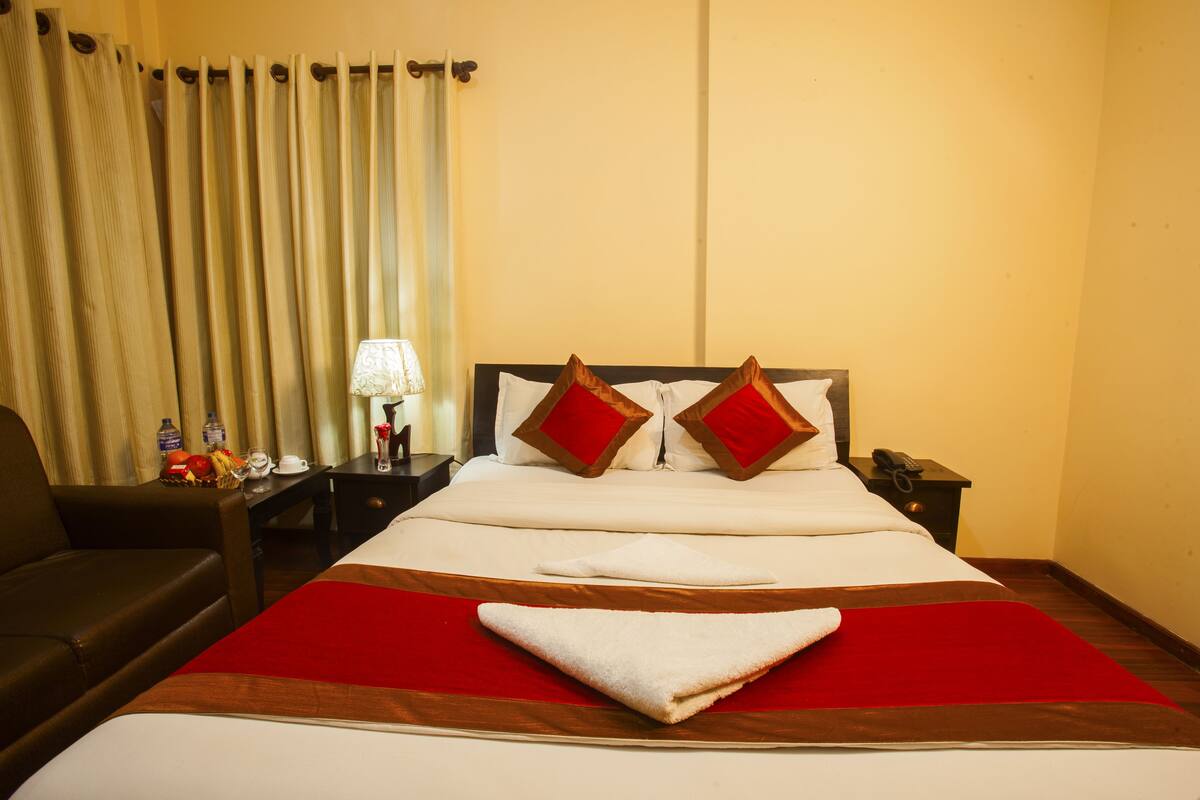 A hotel room with a bed, a nightstand, a lamp, a chair, and a window with curtains.