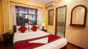 A hotel room with a large bed, a nightstand with a lamp, a window with curtains, a sliding glass door, and a wall-mounted mirror. - Hotel Dream City (Kathmandu)